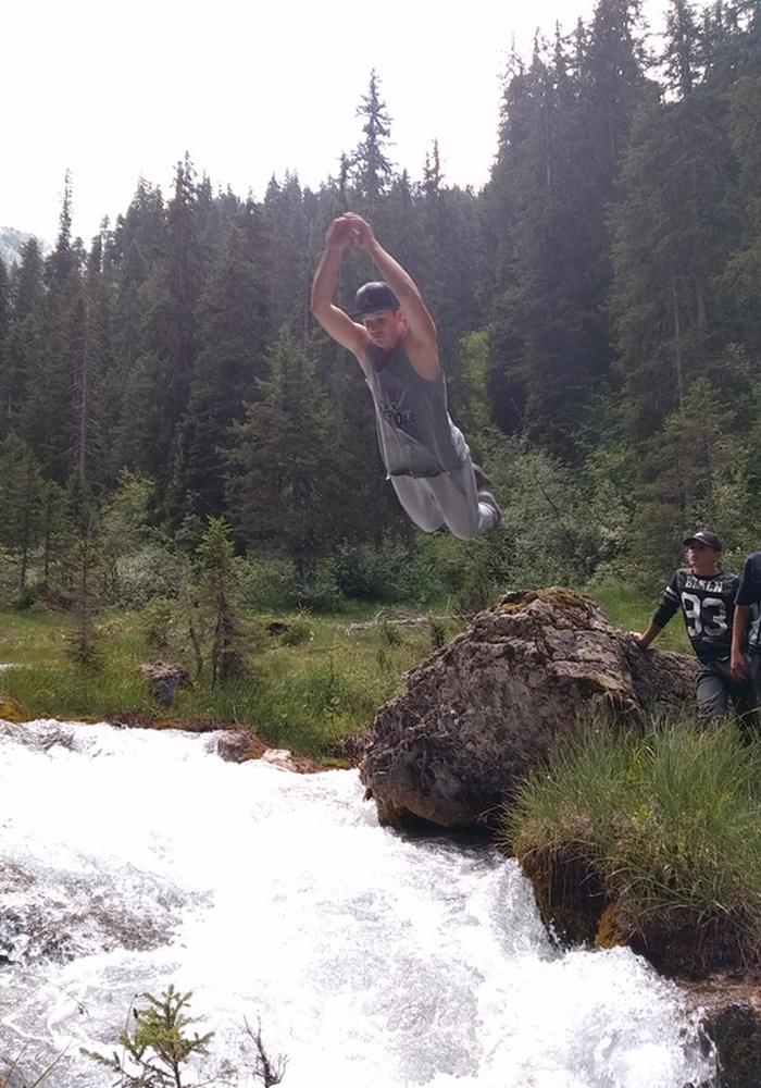 Jeune pratiquant en plein saut au-dessus d'un torrent de montagne